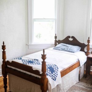 antique wooden bed with a white bedspread, blue and white build near the footboard and a linen bed skirt