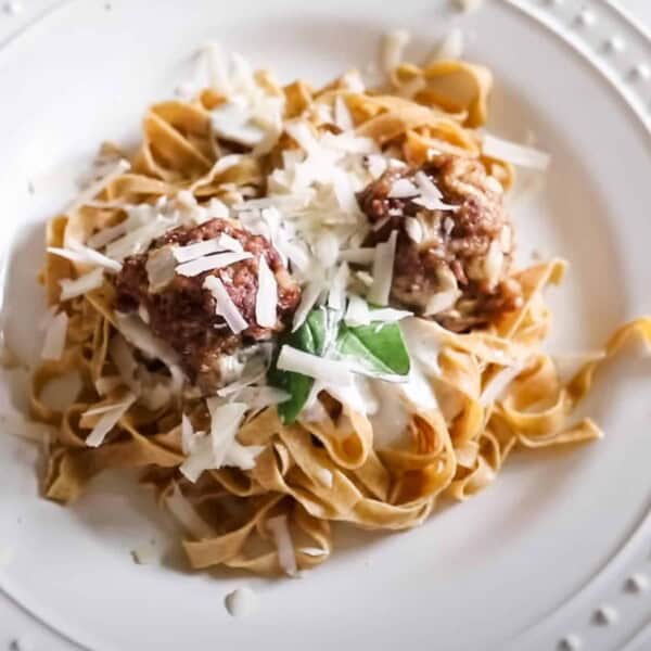 fresh homemade einkorn pasta on a white plate and topped with meatballs fresh herbs and cheese