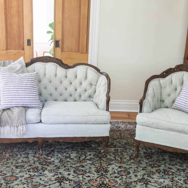 a victorian loveseat and chair freshly painted with chalk paint in a soft green color on a rug with pillows and a blanket draped over