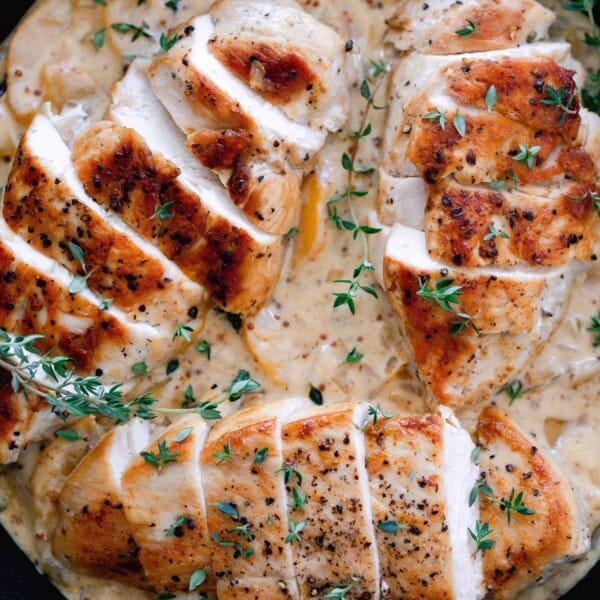 overhead photo of seared and sliced chicken breasts on top a creamy peach sauce with fresh sprigs of thyme