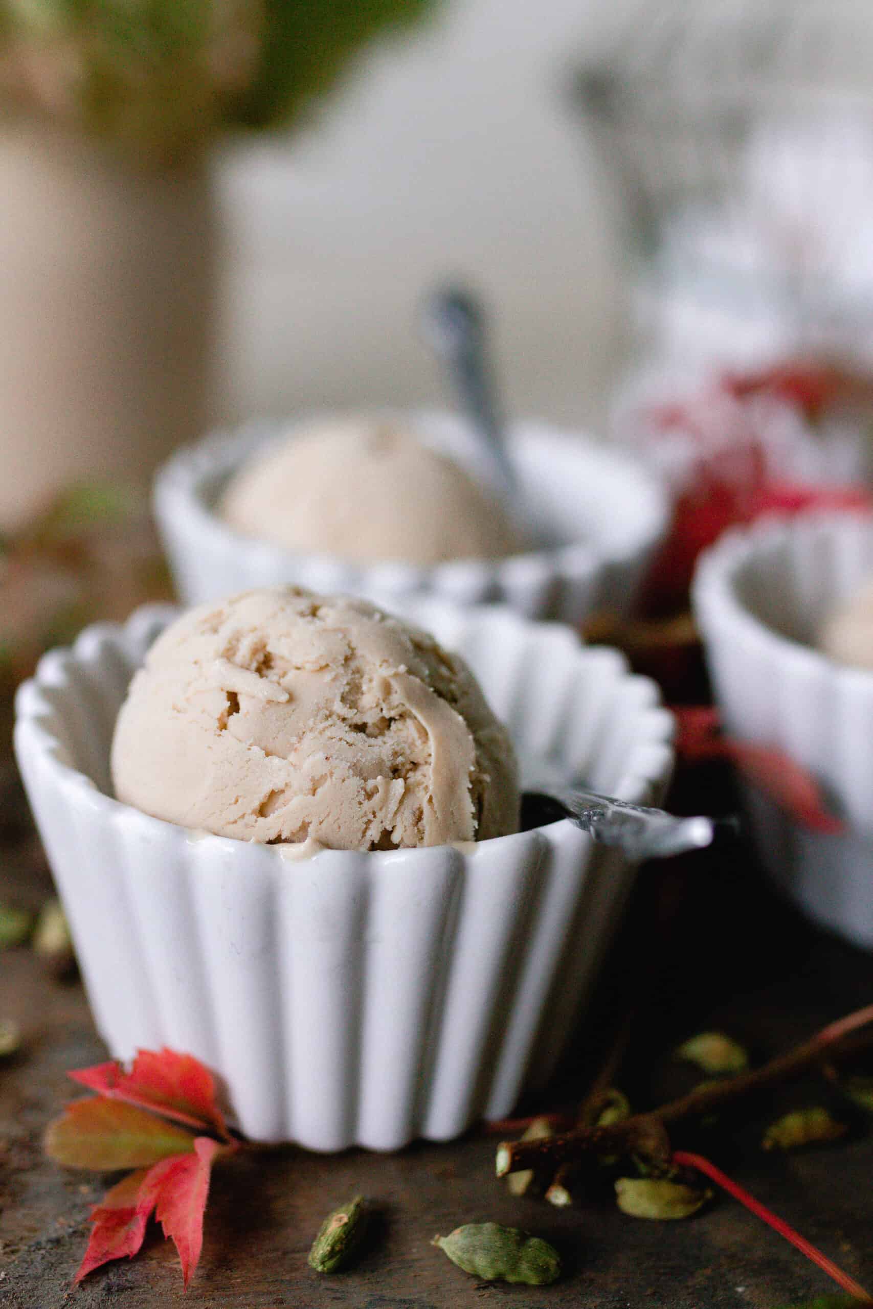 chai ice cream in white bowls with spoons. Red fall leaves are set on the table.