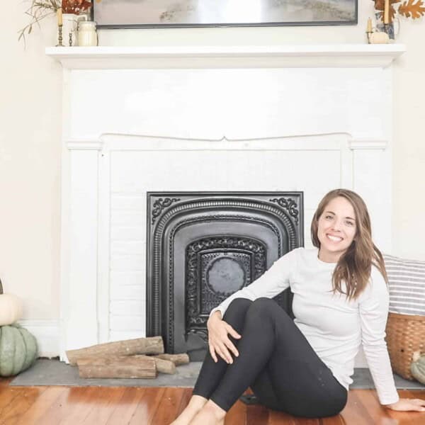 women sitting in front of a white DIY faux fireplace with pumpkins around on the floor