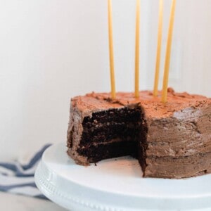 sourdough chocolate cake with chocolate frosting and 4 long beeswax candles on a white cake stand