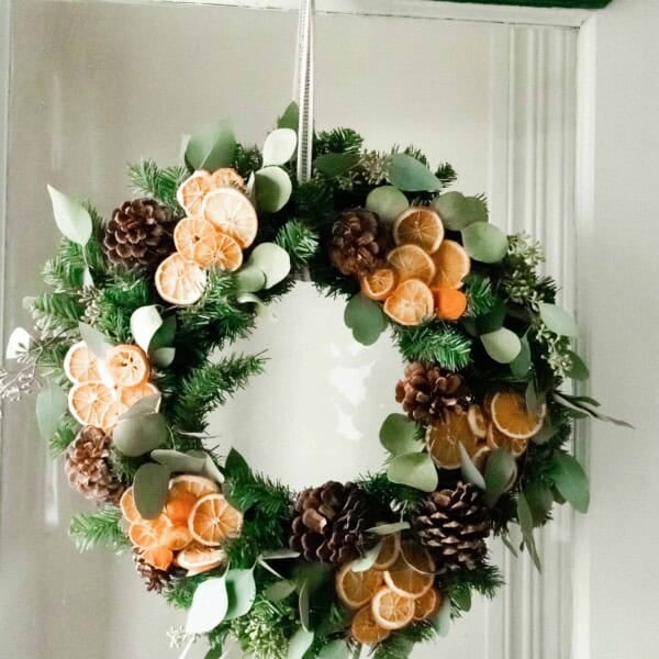 Dried orange and eucalyptus Christmas wreath hanging on a vintage white and green door with glass