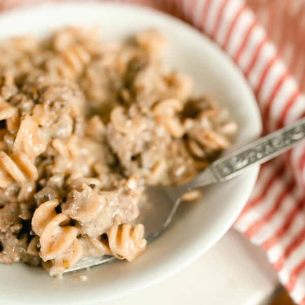 homemade hamburger helper in a white bowl with a fork in the pasta. a red and white stripped napkin to the right