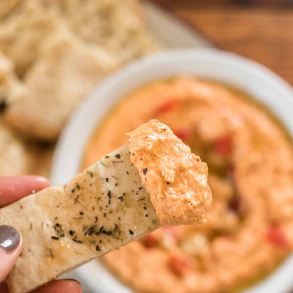 sourdough flat bread dipped into a bowl of roasted red pepper hummus