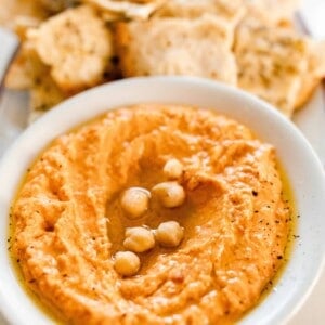 roasted red pepper hummus in a bowl drizzled with olive oil. Sourdough flat bread is in the background