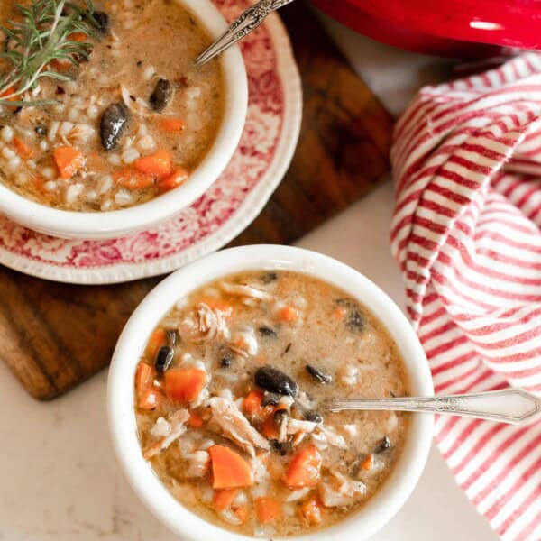 two bowls of chicken Marsala Soup. One bowl is on a red and white antique dish on top a wooden cutting board. A red and white stripped towel sits to the right