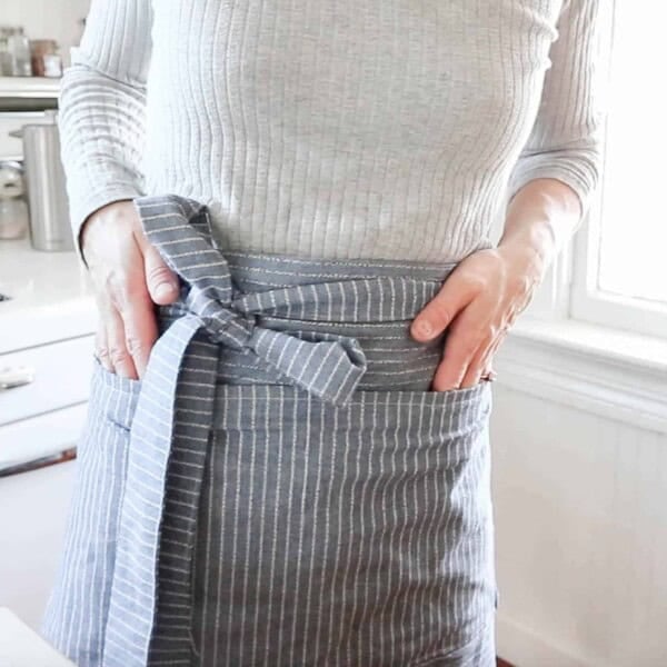 women wearing a gray sweater and wearing a half apron in front of a vintage stove