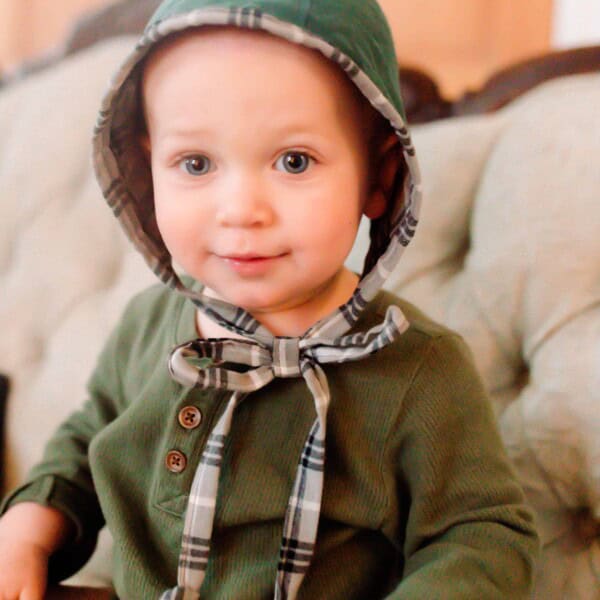 Baby boy in a green shirt wearing a green and plaid homemade bonnet