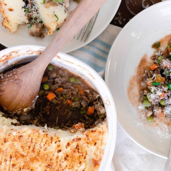 two plates and a baking dish of Shepards pie. Ground beef and veggies topped with mashed potatoes.