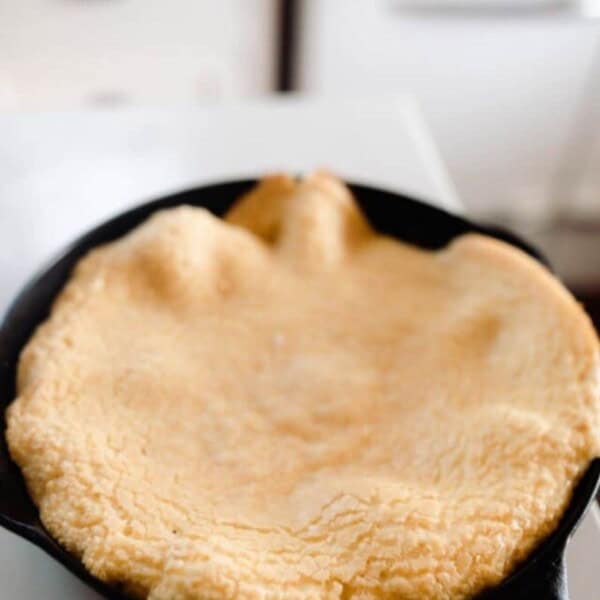 einkorn puff pancake in a cast iron skillet on white quarts countertop. A antique stove is in the background