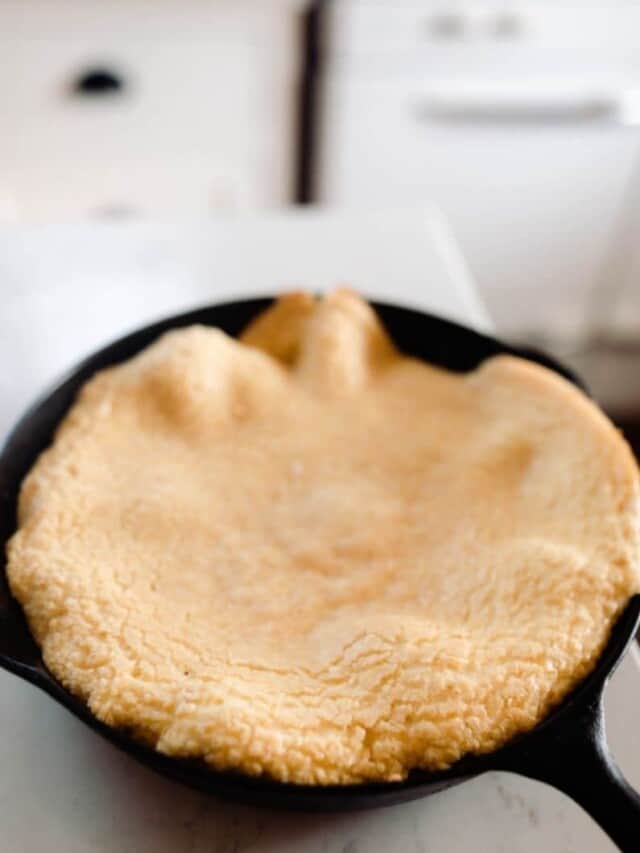 einkorn puff pancake in a cast iron skillet on white quarts countertop. A antique stove is in the background