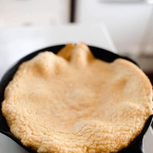 einkorn puff pancake in a cast iron skillet on white quarts countertop. A antique stove is in the background