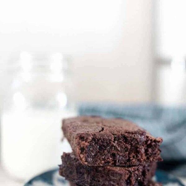 3 einkorn brownies stacked up on a blue and white plate with a glass of milk in the background