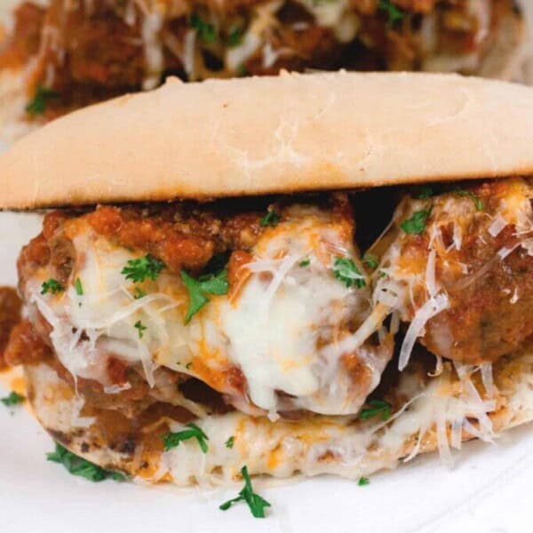 homemade meatball sub sandwich with cheese, marinara sauce, and parsley on a white plate. Another sandwich is in the background