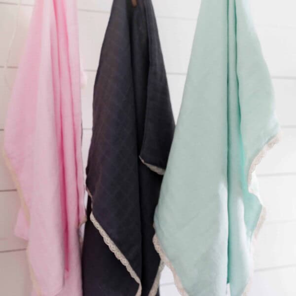 a pink, navy, and teal gauze swaddle blanket with lace hangin with clothespins on string