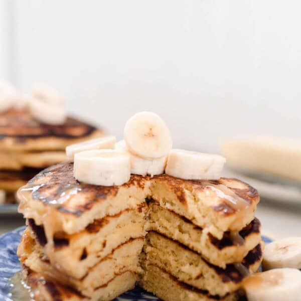 stack of einkorn pancakes topped with bananas on a blue and white antique plate. Butter on a dish is in the background