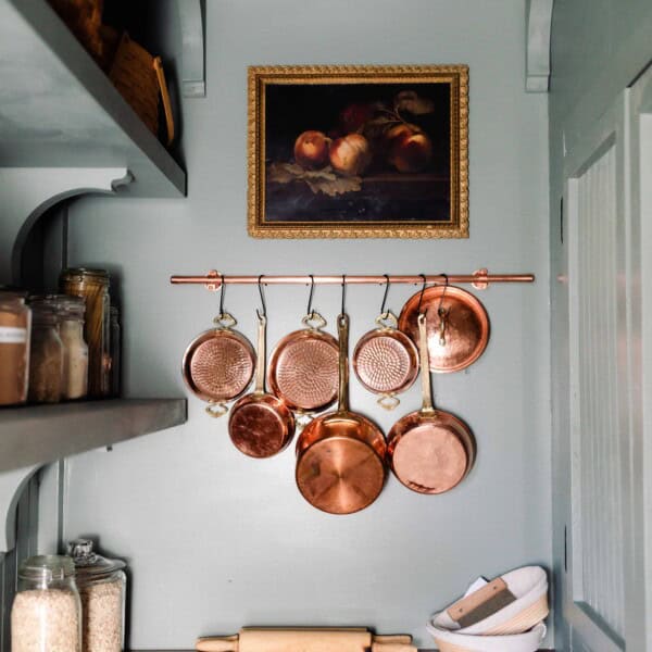 victorian farmhouse pantry with blue green walls, cabinets with wood countertops, shelving, and copper pots handing on the wall