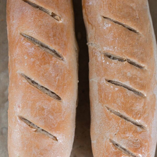 overhead photo of two baked sourdough French breads on parchment paper.