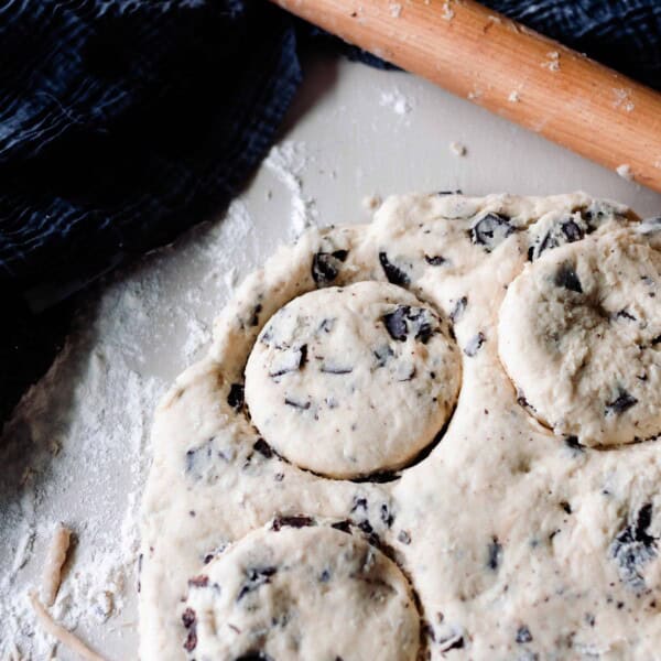 sourdough scone dough rolled out with 3 circles cut out and a rolling pin on a blue towel in the background