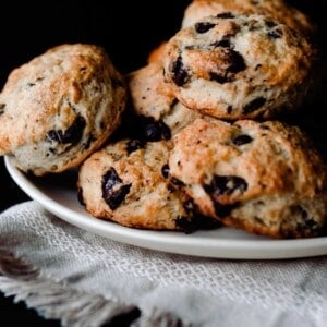 sourdough scones with chocolate chips and coconut stacked on a cream colored plate on a cream colored woven towel