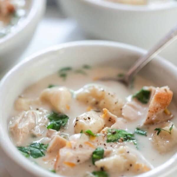 creamy gnocchi soup with chicken and herbs in a white bowl with a spoon in the soup. More bowls of soup in the background