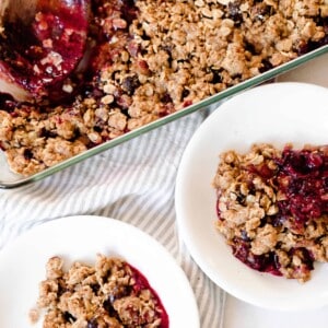 overhead photo of two white bowls filled with einkorn berry crisp with a baking dish of crisp behind the bowls in a background