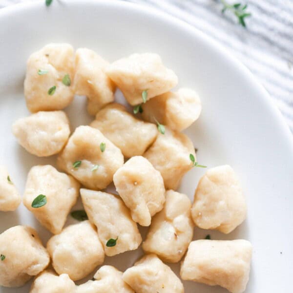 overhead photo of homemade gnocchi in a white bowl with thyme on top of a blue and white stripped napkin in the background