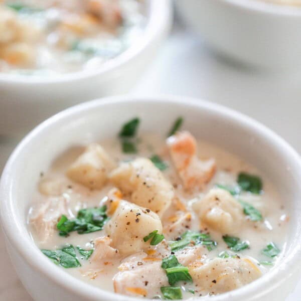 three white bowls filled with homemade gnocchi soup topped with fresh herbs on a white and gray quarts countertop