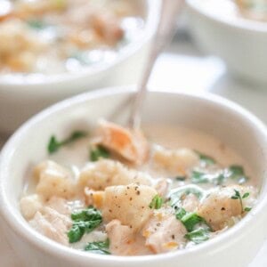 a bowl of creamy chicken and gnocchi soup in a white bowl with a spoon. More bowls of soup are in the background