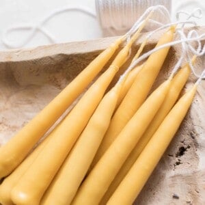 seven hand dipped tampered beeswax candles laying in a wooden bowl with a spool of wick behind the bowl