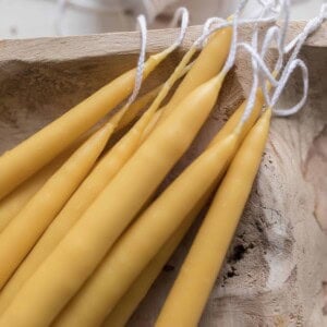 dipped beeswax tapered candles snacked on a wooden bowl with a spool of wick in the background