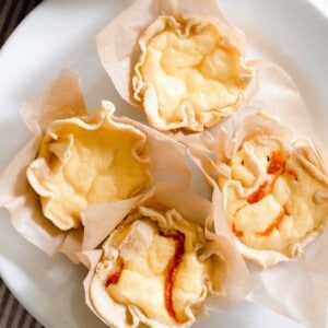 overhead photo of four mini quiches: two just plain with cheese, and two with roasted red pepper and onion) on a white plate