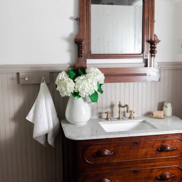 Antique dresser turned into a vanity with a marble tub with a ornate wood mirror. Bead board graces the walls and antique accessories