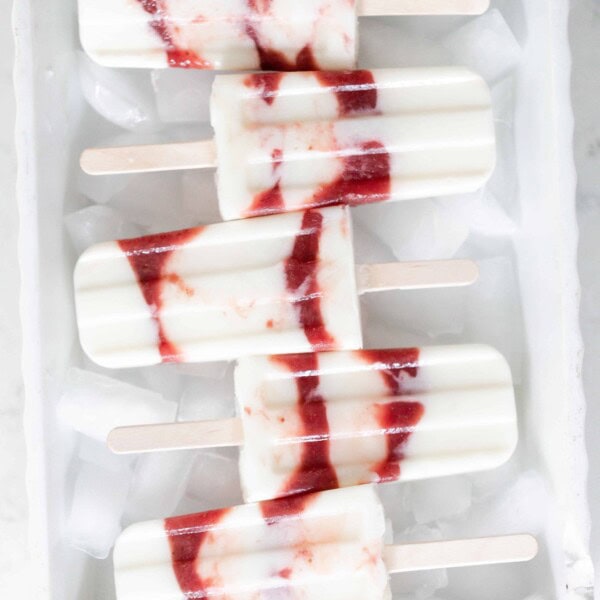 five strawberry yogurt popsicles laying on top of ice cubes in a white dish