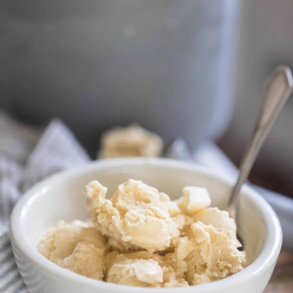 raw milk ice cream in a white bowl with a spoon on a wooden table with the ice cream canister in the background