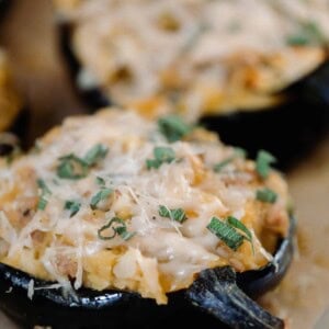 two stuffed acorn squashes topped with cheese on a wood cutting board