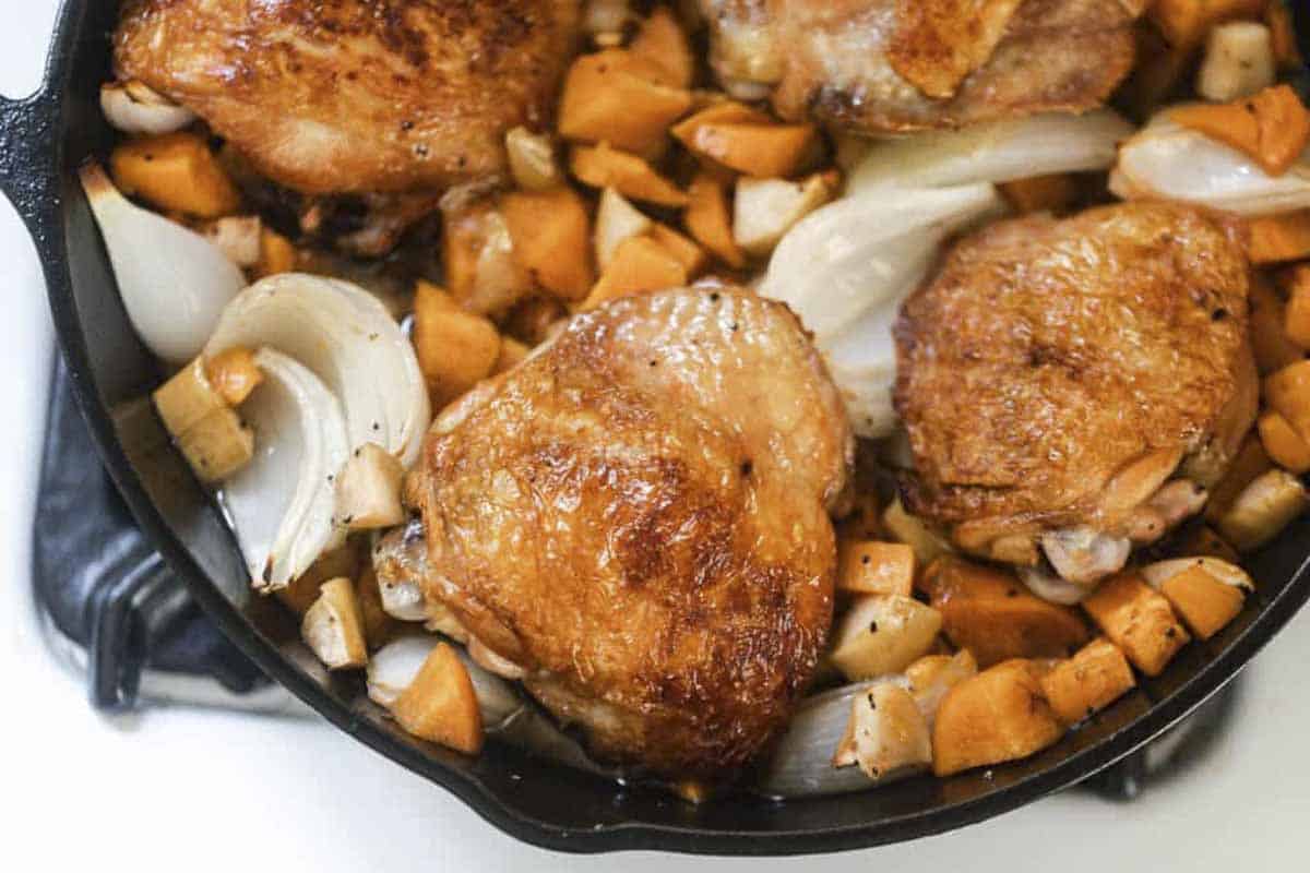 maple roasted chicken with sweet potatoes, onions, and apples in a cast iron skillet.