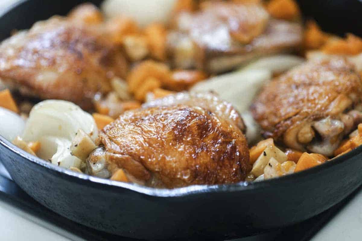 crispy chicken thighs with sweet potatoes, onions, and apples in a cast iron skillet and topped with thyme.