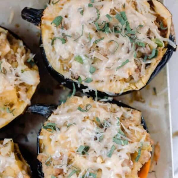 overhead photo of Sausage and Apple Stuffed Acorn Squash topped with parmesan and fresh sage on parchment paper