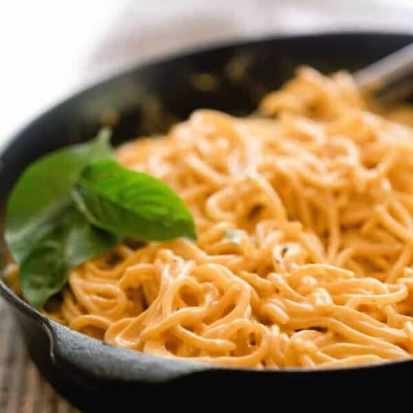 a cast iron skillet with spaghetti topped in pumpkin pasta sauce with fresh basil leaves on top