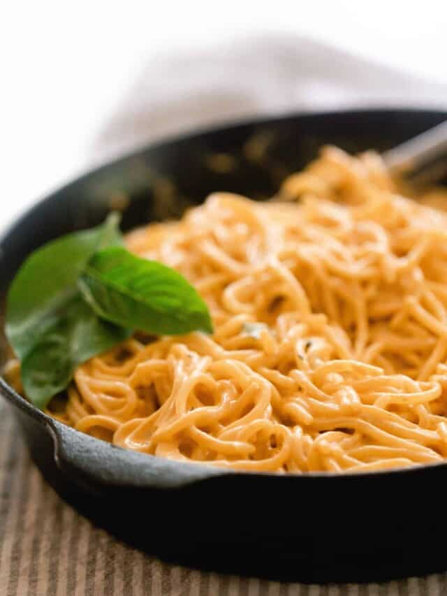 a cast iron skillet with spaghetti topped in pumpkin pasta sauce with fresh basil leaves on top