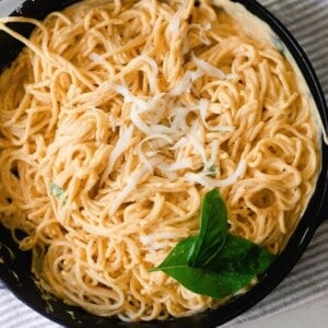 creamy pumpkin pasta sauce with spaghetti noodles mixed in in a cast iron skillet and garnished with basil. The skillet is placed on a white and gray quartz countertop