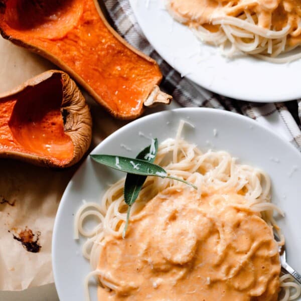 two plates our pumpkin squash pasta sauce over spaghetti with two halves of butternut squash to the side