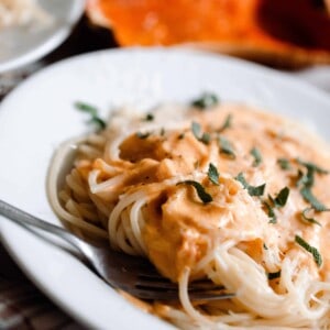 butternut squash pasta sauce poured on top of spaghetti and garnished with fresh herbs. A halved butternut squash is in the background