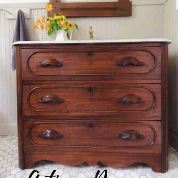 stained wooden antique dresser turned into a bathroom vanity with a marble top. A antique mirror hangs over the vanity.