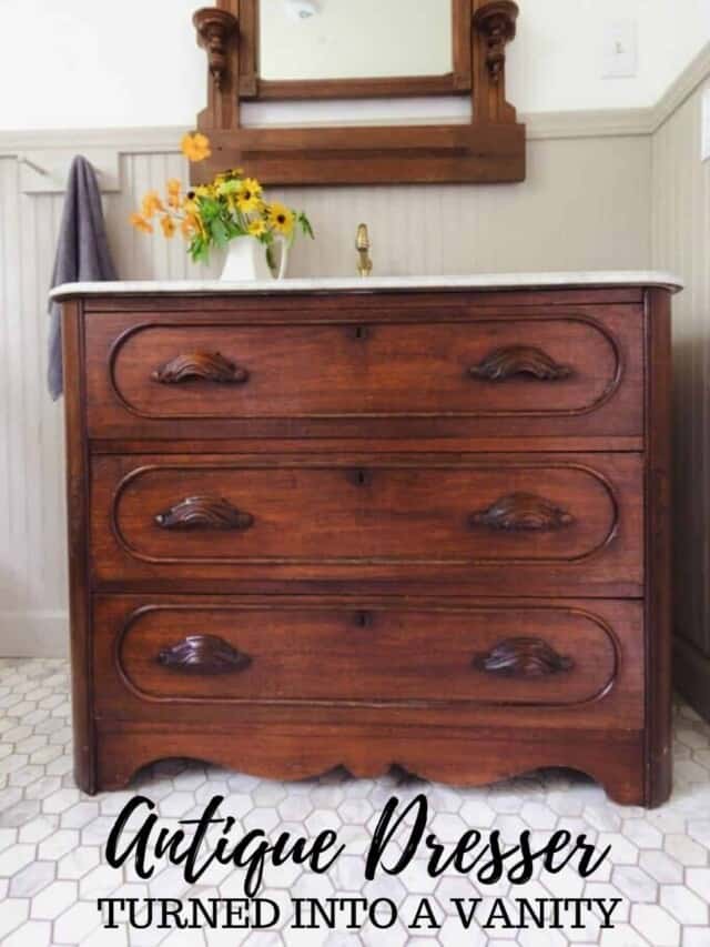 stained wooden antique dresser turned into a bathroom vanity with a marble top. A antique mirror hangs over the vanity.