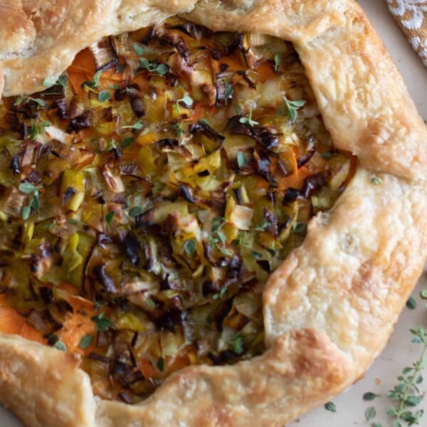 overhead photo of a sourdough galette with leeks and sweet potatoes on a marble countertop with herbs sprinkled around