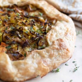 savory sourdough galette on a marble countertop with fresh thyme sprinkled around. A towel is in the background